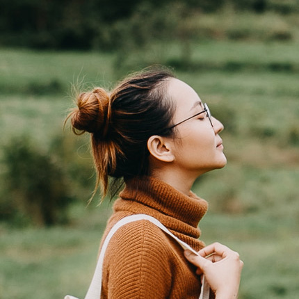 Perfil lateral de una mujer con jersey de cuello alto de color rojizo y bolso blanco. Mira hacia arriba con los ojos cerrados.